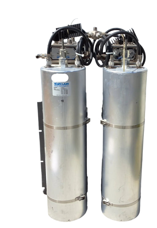 Two cylindrical metal tanks with piping and valves on a concrete surface.